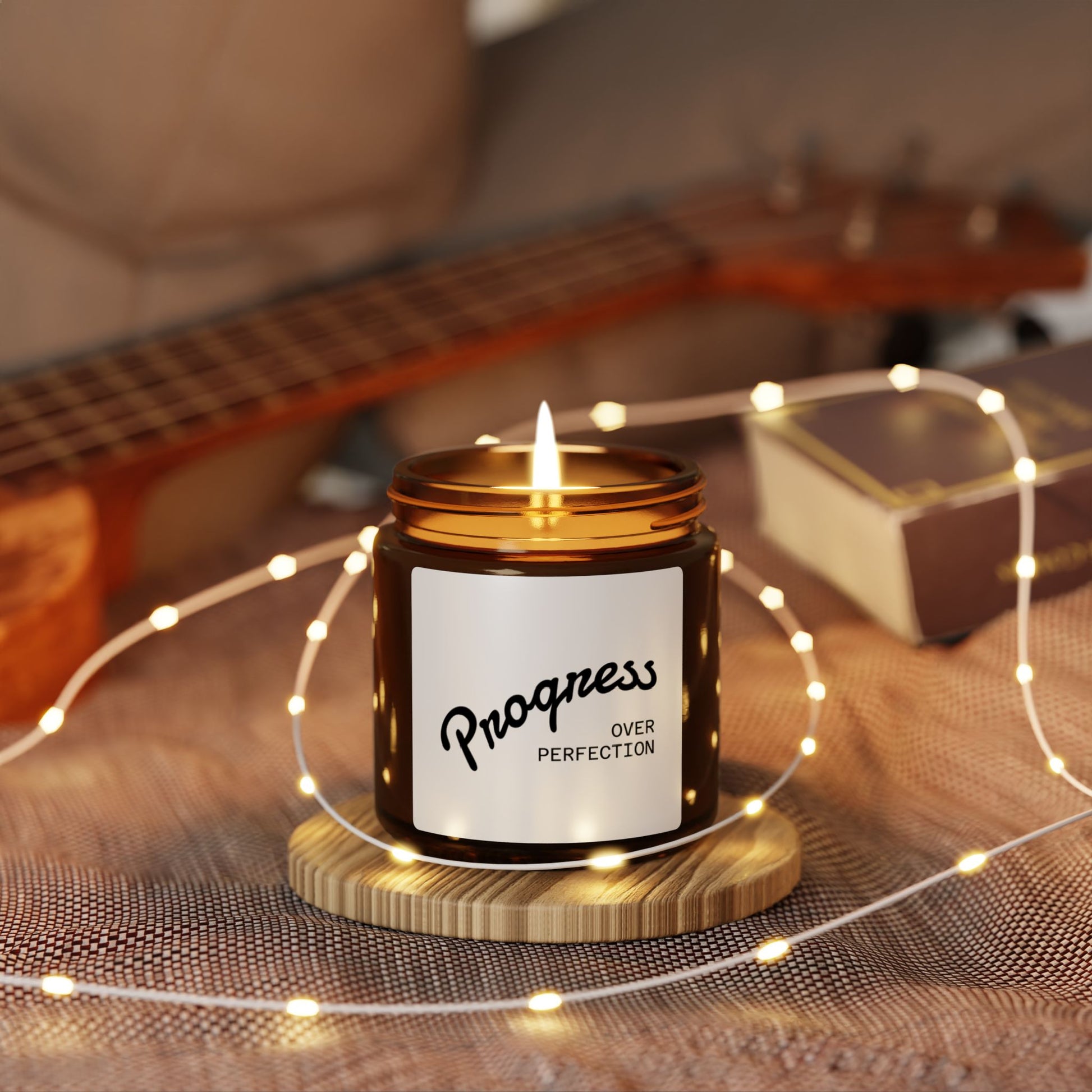 Progress Over Perfection scented candle burning on cozy table with fairy lights  and a guitar in the background motivational home decor
