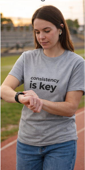 Woman wearing Consistency is Key motivational t-shirt outdoors checking fitness watch.