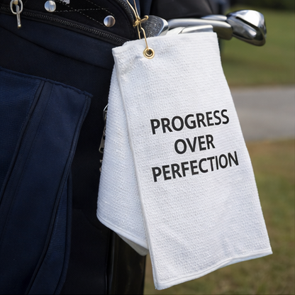 White towel with 'Progress Over Perfection' text hanging on a golf club