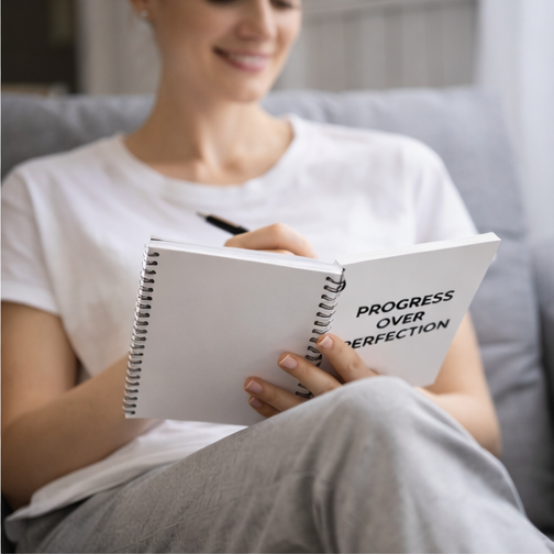 Woman holding Progress Over Perfection spiral notebook motivational dotted journal