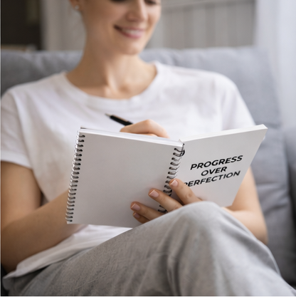 Woman holding Progress Over Perfection spiral notebook motivational dotted journal