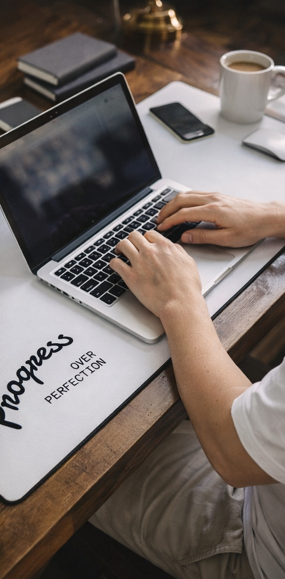 Person working on laptop with Progress Over Perfection desk mat in home office workspace