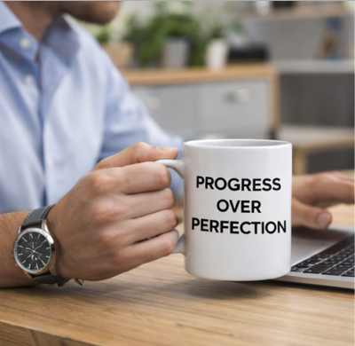 Progress over perfection motivational coffee mug held by professional at desk with laptop, white ceramic cup for home office inspiration
