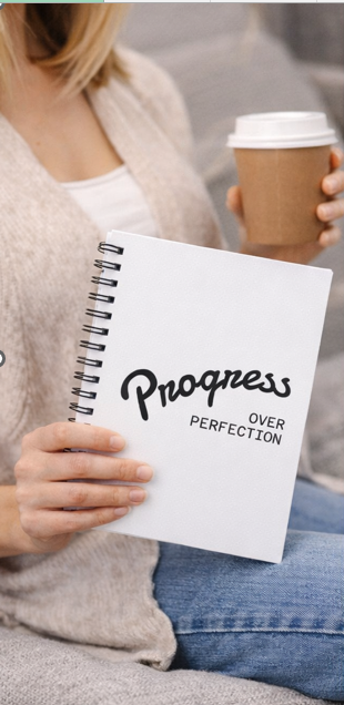 Woman holding progress over perfection spiral notebook with coffee, motivational journal for goal-setting and personal development
