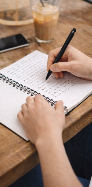 Hand writing in progress over perfection spiral notebook at wooden desk, motivational journal for goal-setting and reflection
