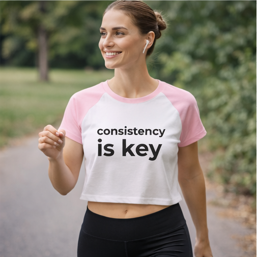 Woman in consistency is key pink crop top during outdoor workout, motivational fitness tee for running and exercise
