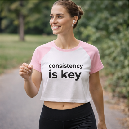 Woman in consistency is key pink crop top during outdoor workout, motivational fitness tee for running and exercise
