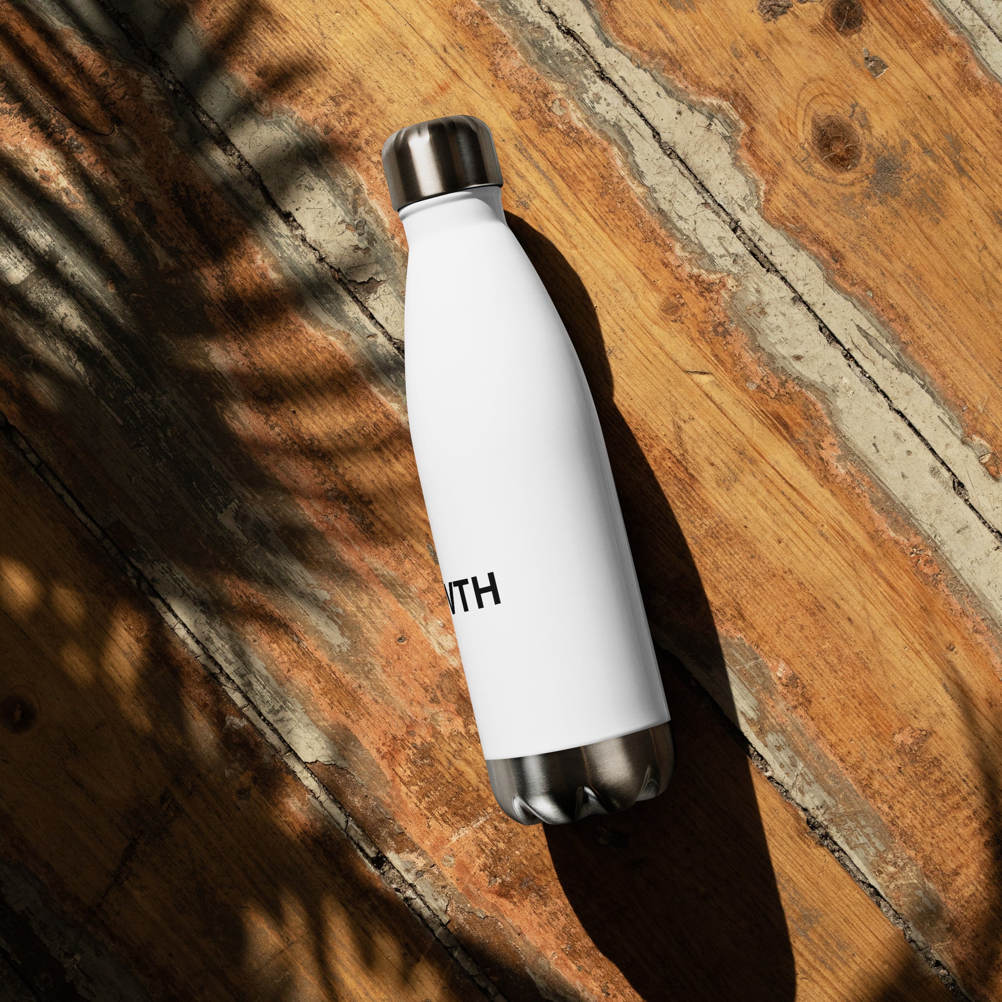 Growth motivational insulated water bottle on wooden surface, white stainless steel bottle for daily hydration and wellness

