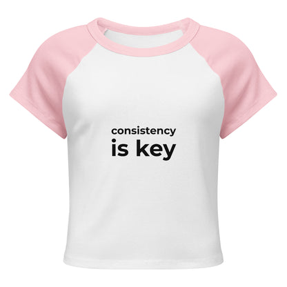 Consistency is key pink and white raglan t-shirt front view, motivational women's apparel with bold black text
